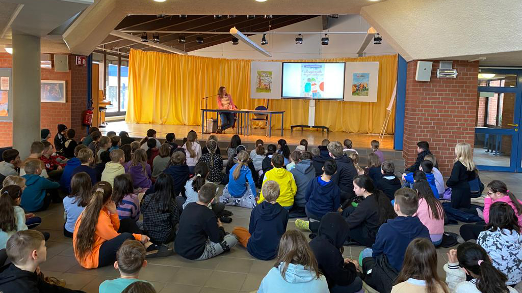 Kinder lauschen einer Autorenvorlesung in der Aula